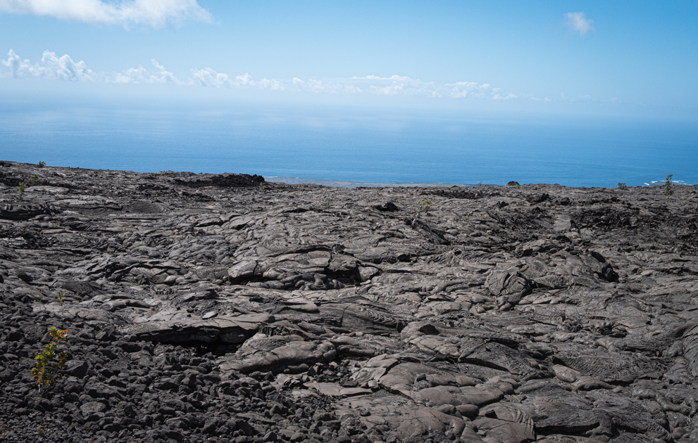 Hardened black lava flows stretching from volcanic slopes down to the Pacific Ocean at Hawai‘i Volcanoes National Park.
