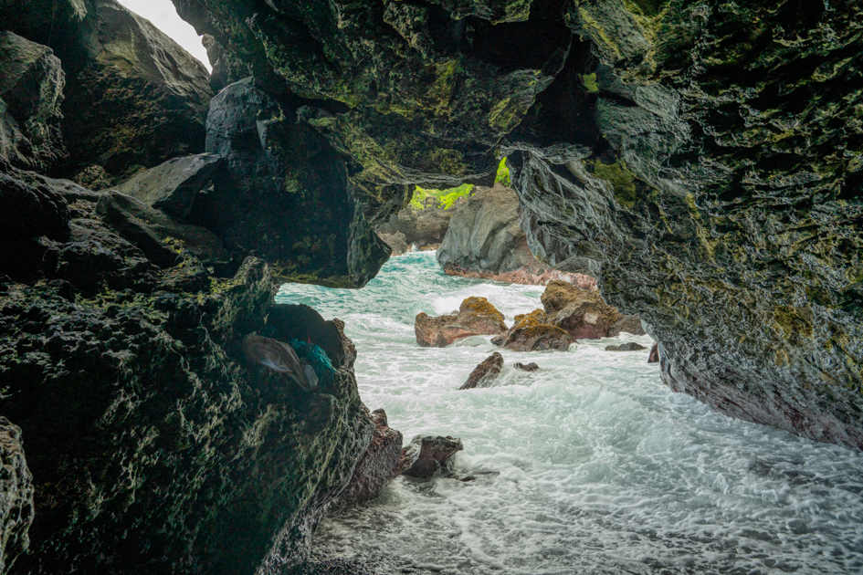Inside a Hawaiian lava tube with ocean view and skylight opening in the ceiling revealing the sky through volcanic rock.