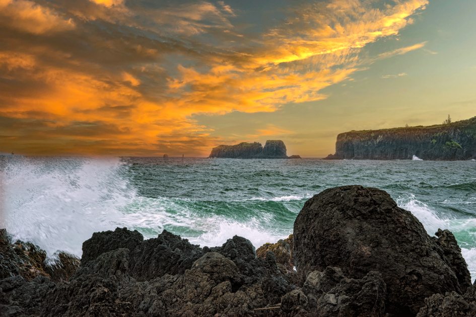Black lava rocks along the coastline at sunset, with the cliff in the distance where Steve McQueen's character jumps in the movie Papillon, glowing under golden skies.