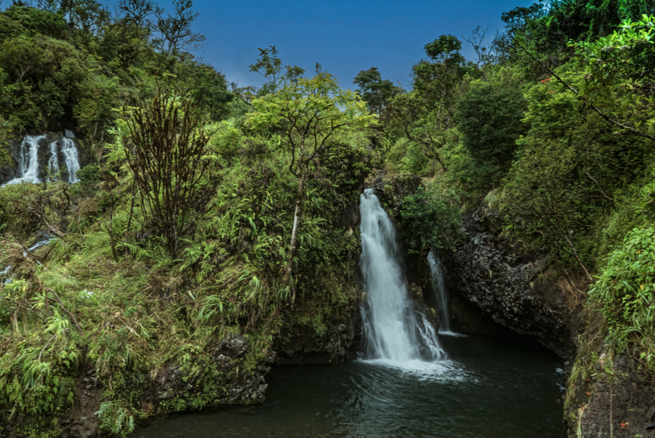 Two waterfalls flowing side by side through dense, tropical greenery, surrounded by moss-covered rocks and vibrant jungle foliage.