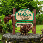 A green roadside sign that reads “Welcome to Hana,” marking the entrance to the town at the end of Maui’s iconic Road to Hana scenic drive.