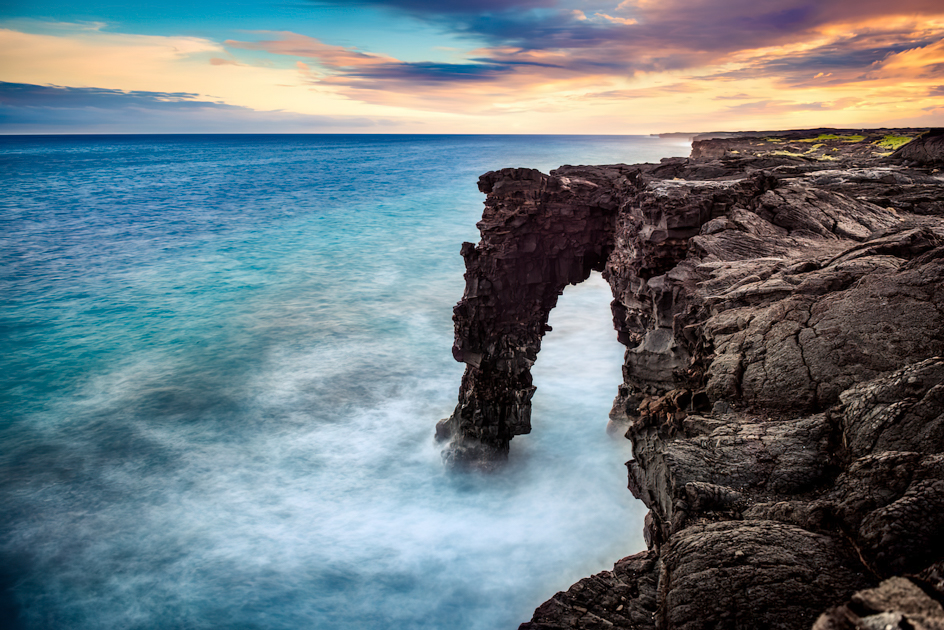 The Hōlei Sea Arch silhouetted against a colorful sunset sky at Hawai‘i Volcanoes National Park.