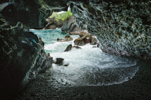 Inside a lava tube in Hawaii with a view looking out toward the ocean framed by volcanic rock.