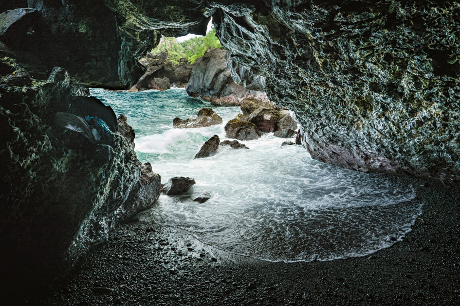 Inside a lava tube in Hawaii with a view looking out toward the ocean framed by volcanic rock.