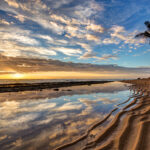 Sunset at Kapaa Beach in Kauai with golden light reflecting on the ocean and palm trees silhouetted against the sky. travel blogs, travel photography photography trvel blog, back roads lens. Kauai travel guide