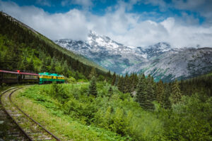 The White Pass and Yukon Railroad train rounding a curve with towering mountains in the background near Skagway, Alaska. Alaska travel guide