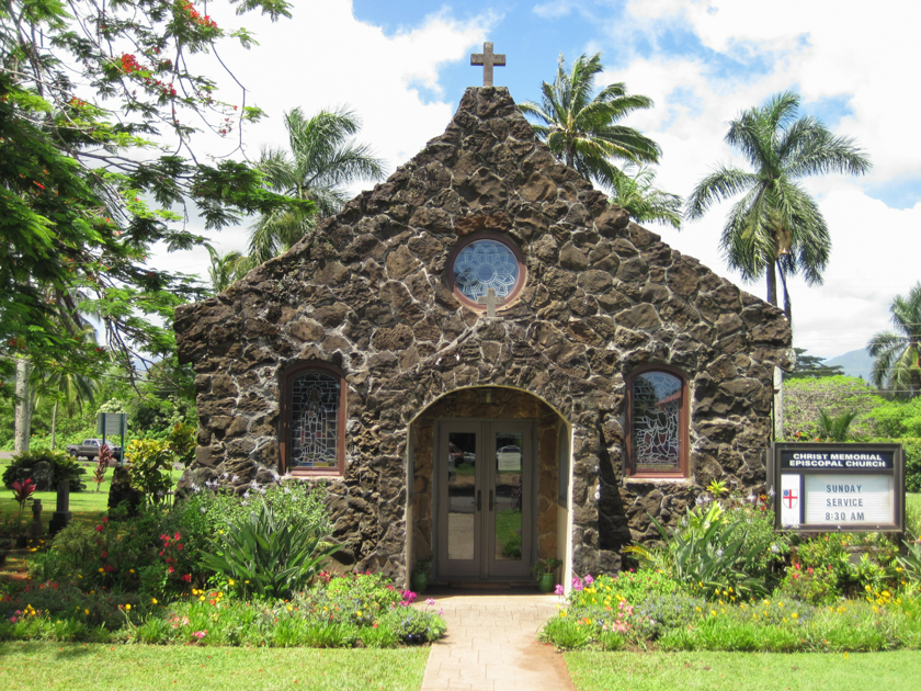 View of Christ Memorial Episcopal Church on Kauai, showing the wooden chapel surrounded by tropical vegetation.