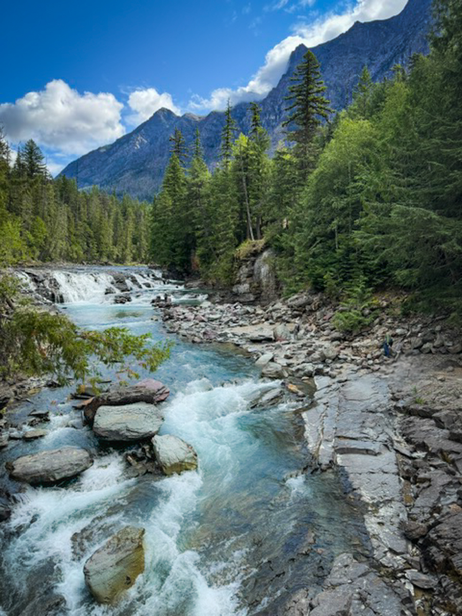 A serene river flowing through Glacier National Park, with towering mountains rising in the background.