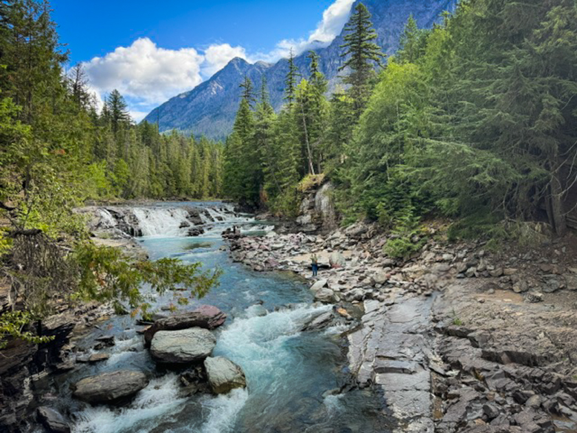 Waterfall flowing in the foreground with majestic mountain peaks in the background in Glacier National Park