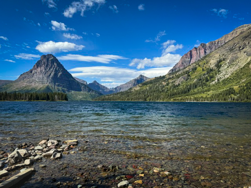 Calm waters of Two Medicine Lake reflecting mountain peaks and sky in Glacier National Park