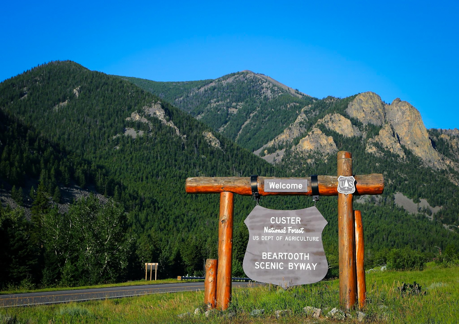 Beartooth Highway entrance sign with mountains and open sky in the background, marking the start of a scenic alpine drive.