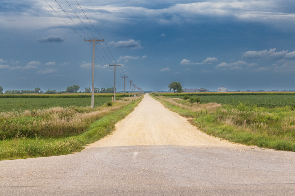 "Gravel side roads branching off a paved rural highway in Iowa under a wide open sky"