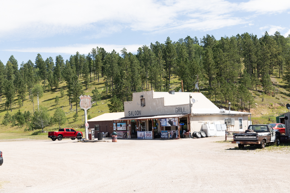 Rustic exterior of Buckhorn Bar and Grill in Buckhorn, Wyoming, featuring a vintage gas pump, old weathered sign, and wooden building