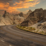 Winding road through the dramatic landscape of Badlands National Park, glowing under a colorful sunset sky.