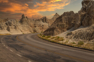 Winding road through the dramatic landscape of Badlands National Park, glowing under a colorful sunset sky.