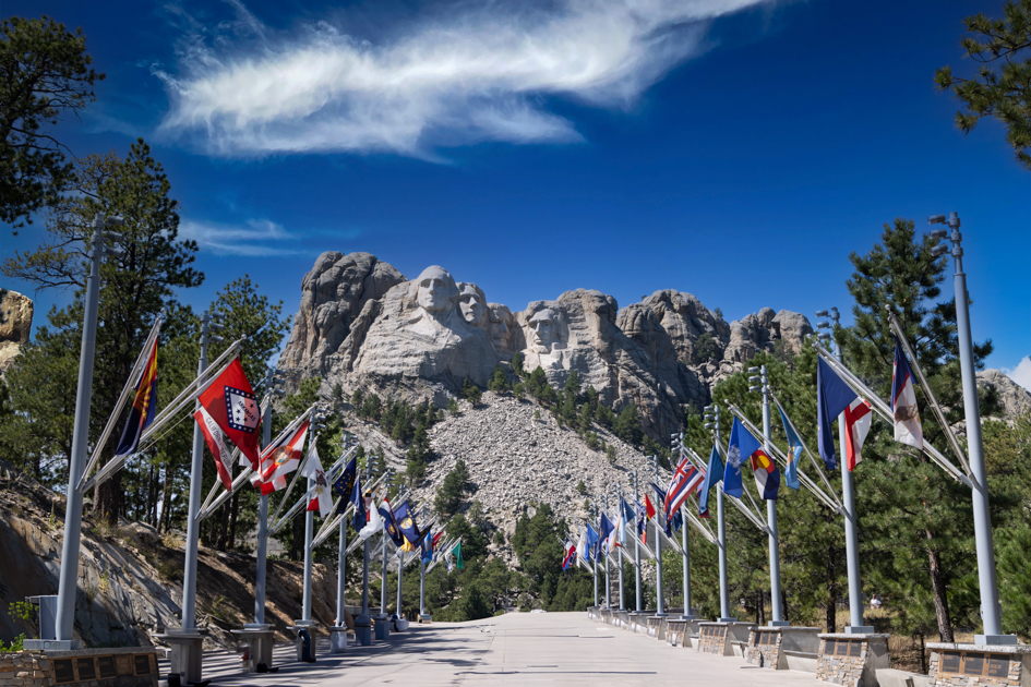 View of Mount Rushmore with American flags lining the Grand View Terrace walkway, captured at golden hour in South Dakota's Black Hills.