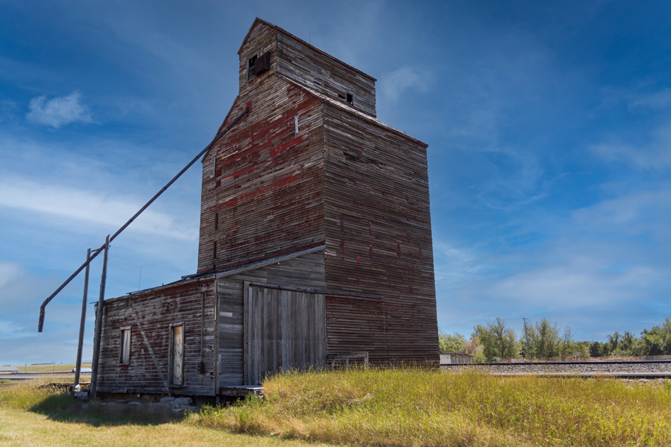 Weathered wooden grain silo standing alone in a rural Montana field under an overcast sky