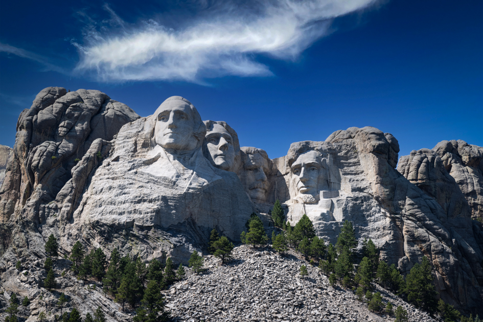 Mount Rushmore in South Dakota, with clear blue skies and the carved faces of four U.S. presidents illuminated by warm golden hour light.