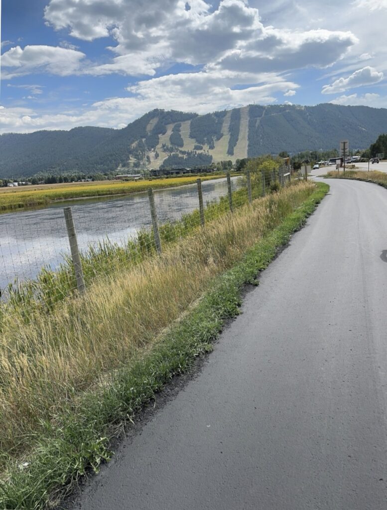 Bike trail leading toward Jackson, Wyoming, with green ski slopes visible on the mountains in summer