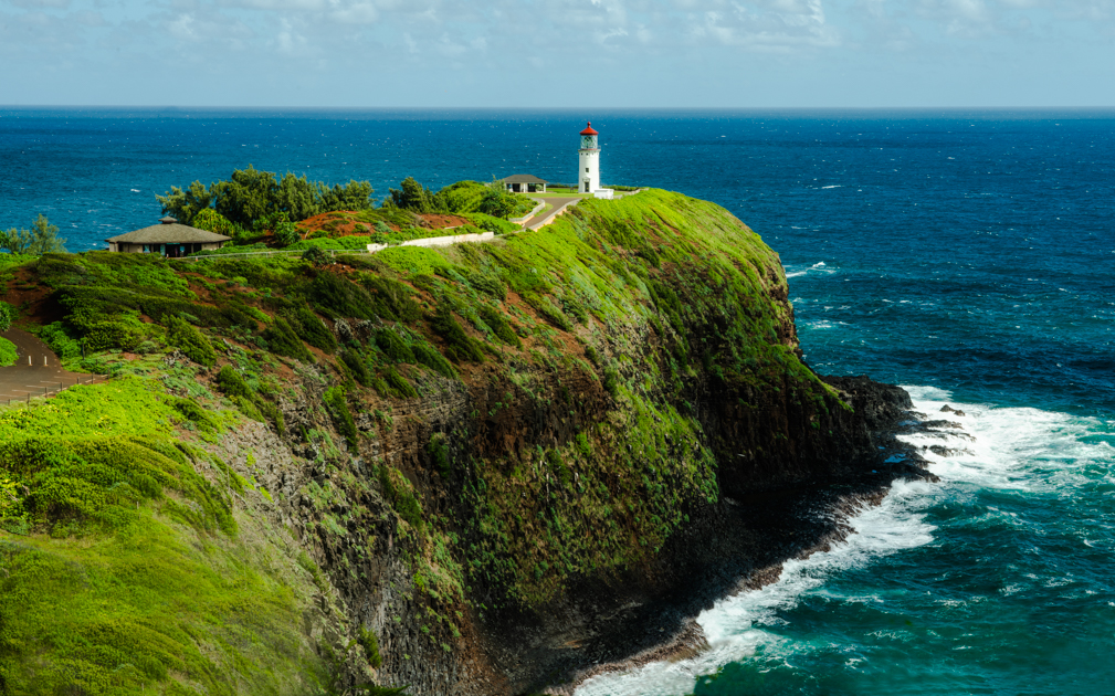 Kilauea Lighthouse on Kauai perched on a cliff, overlooking the Pacific Ocean with waves crashing below.