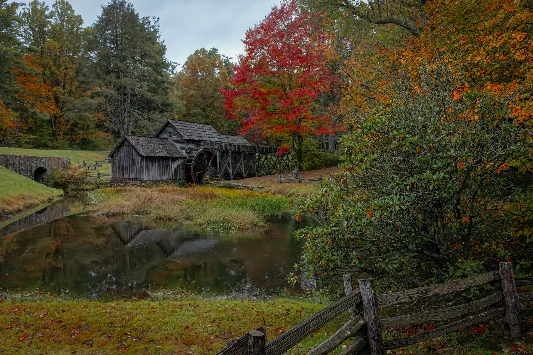 Old mill with fall colored trees surrounding it and a rustic wooden fence. Fall photography, seasons photography