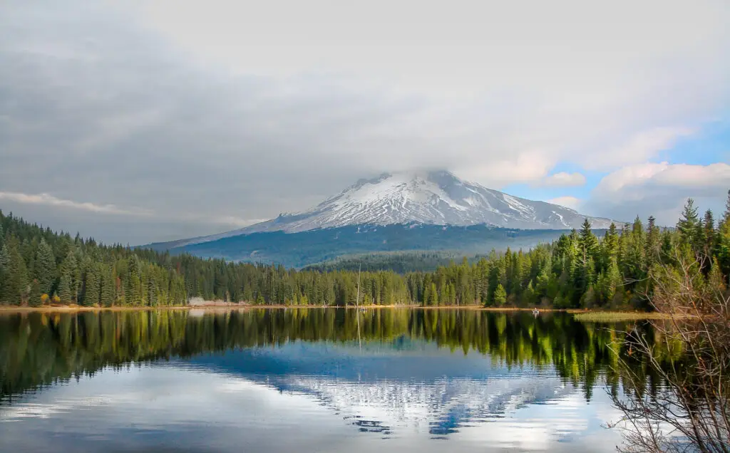 Mount Hood at Trillium Lake with reflections of the mountain in the lake. The mountain has snow capped peaks and lake is surrounded with evergreen trees