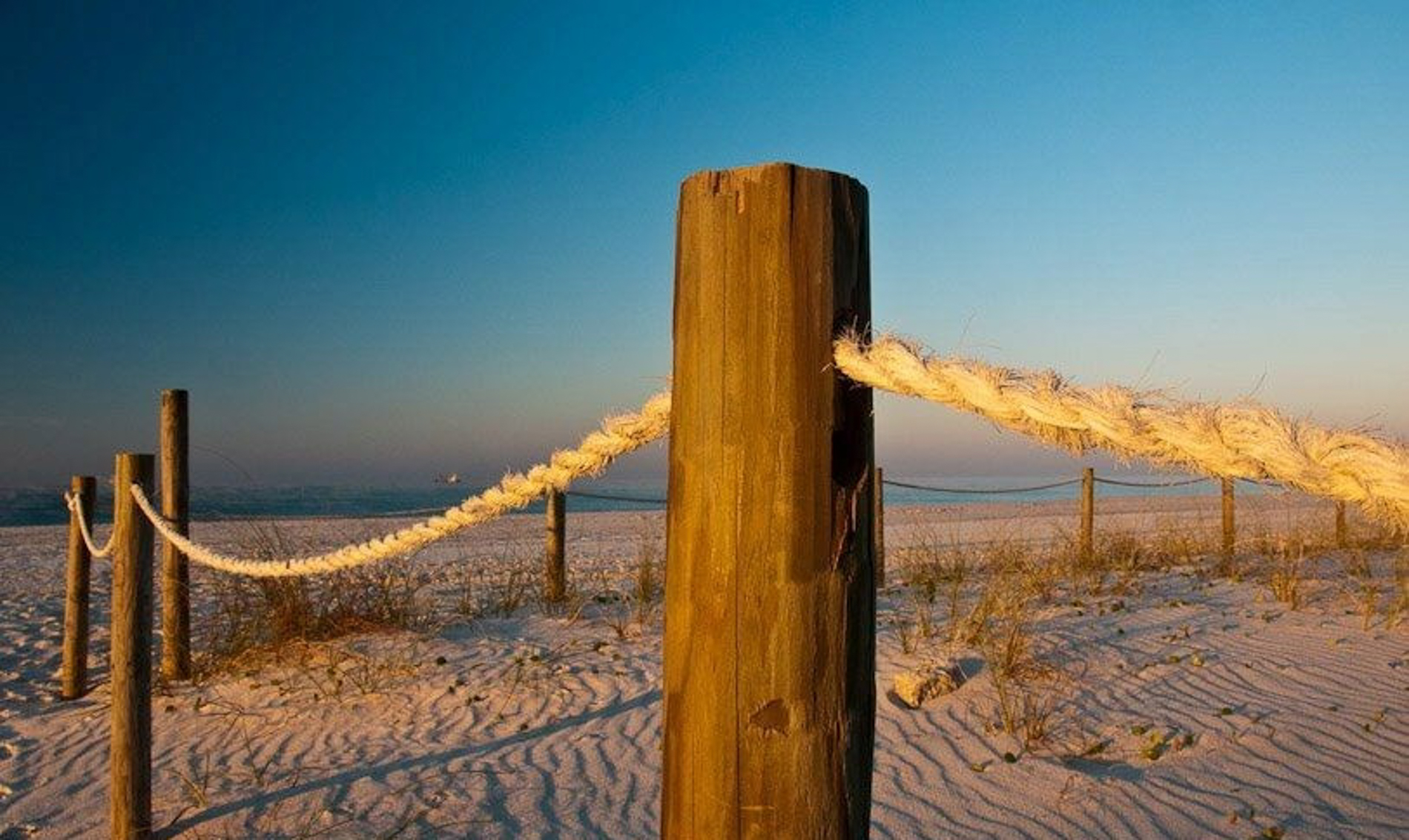 Weathered wood posts with rope along a sandy beach, creating a rustic coastal barrier. coastal travel photography