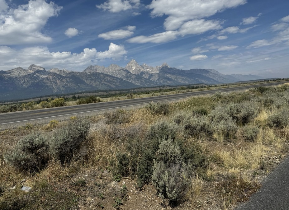 Paved bike trail winding through open landscape with the Grand Teton mountains in the distance