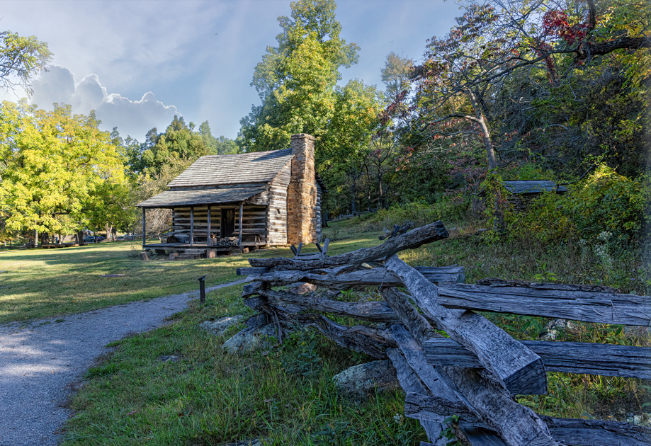Log cabin and split-rail fence at Humpback Rocks Mountain Farm, surrounded by trees and Appalachian landscape.
