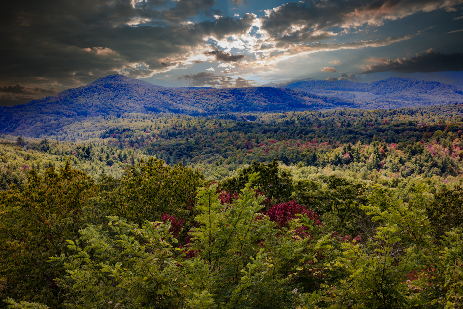 Layered mountain ridges leading to Mount Mitchell under a hazy blue sky, viewed from Milepost 349.9 on the Blue Ridge Parkway.
