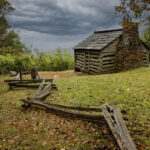 Historic 1880s log cabin known as Trail Cabin, surrounded by grass and trees along the Blue Ridge Parkway at Milepost 154.