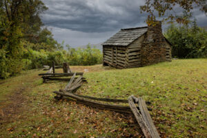 Historic 1880s log cabin known as Trail Cabin, surrounded by grass and trees along the Blue Ridge Parkway at Milepost 154.