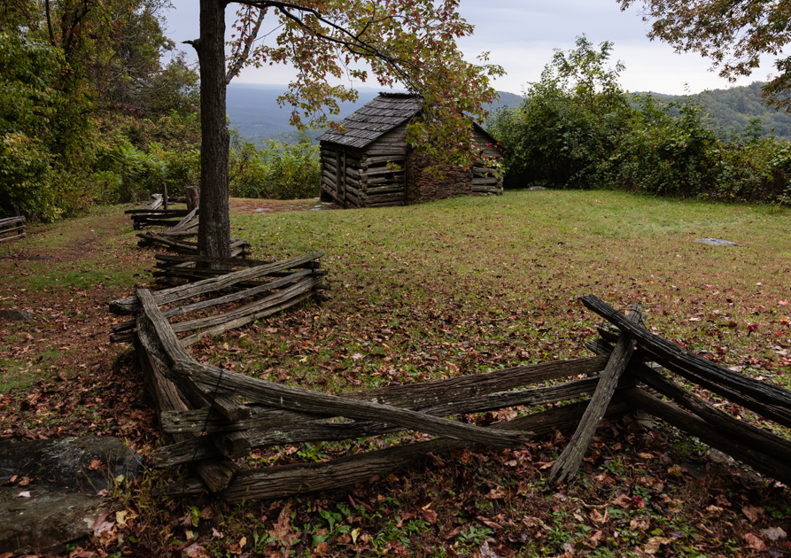 view of the 1880s Trail Cabin with weathered logs and a sloped roof, nestled in the Appalachian landscape along the Blue Ridge Parkway.