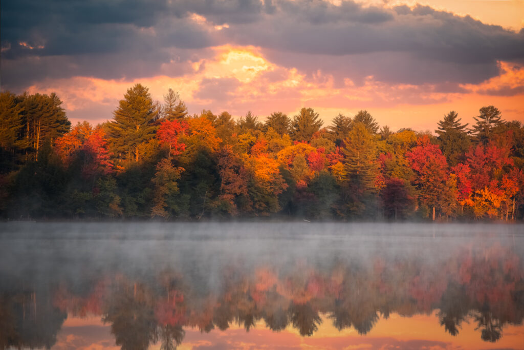 Fall sunrise over White Lake in the Adirondack Mountains with colorful trees reflected in the calm water