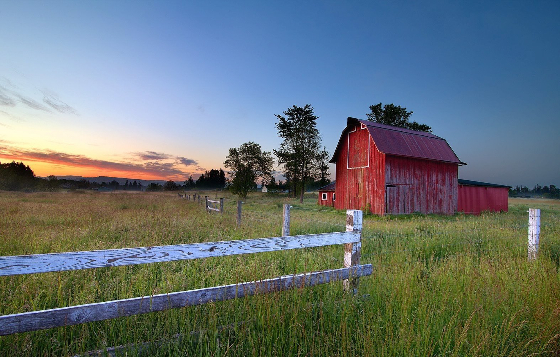 Red barn with white picket fence glowing in the light of a country sunset