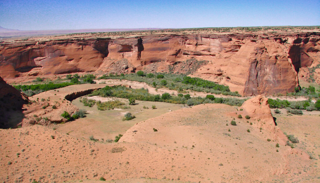 Canyon de Chelly valley floor with Navajo farms and steep red sandstone canyon walls in Arizona.