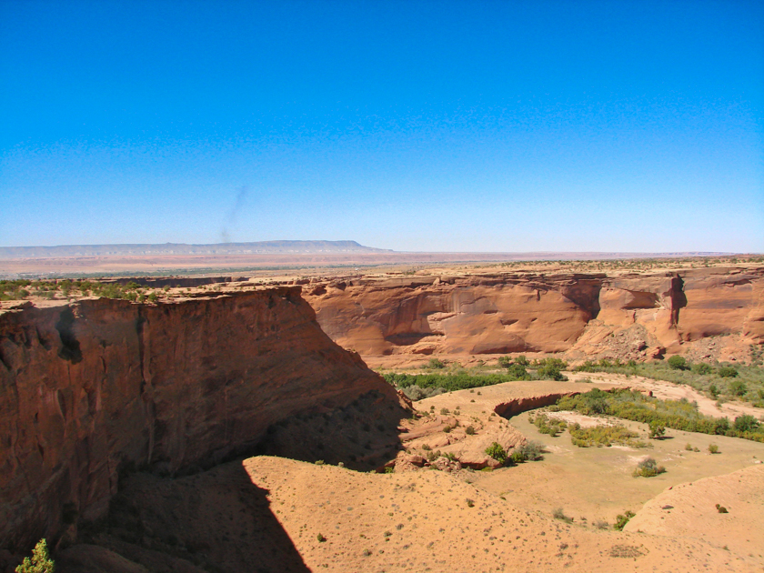 Wide view of Canyon de Chelly showing the valley floor and towering red sandstone canyon walls in Arizona.
