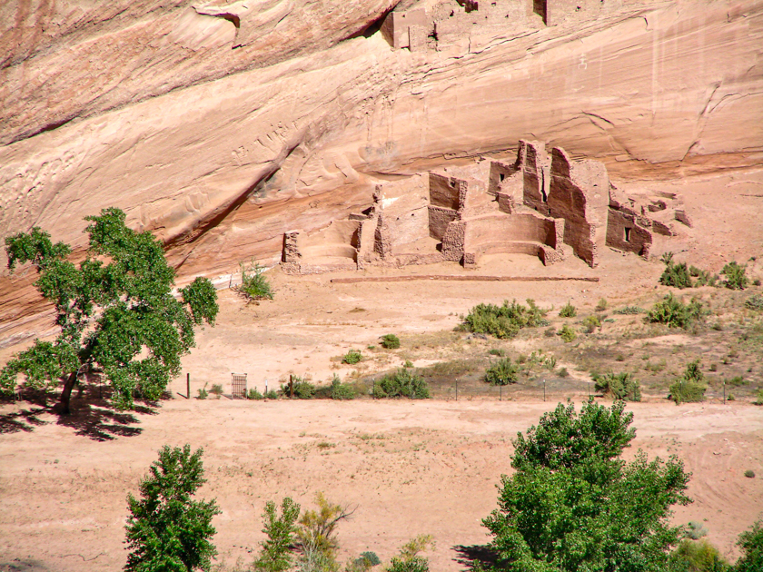 Stone cliff dwellings of Canyon de Chelly set against red sandstone cliffs in Arizona.