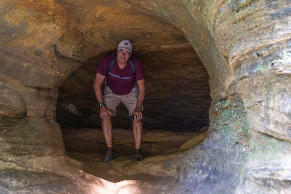A man standing at the entrance of Old Man’s Cave in Hocking Hills, Ohio, surrounded by rugged stone walls.
