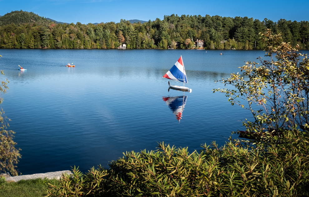 Sailboat on Mirror Lake in Lake Placid with its reflection in the water.
