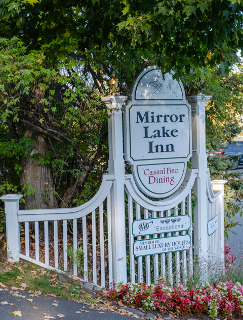 Mirror Lake Inn sign in Lake Placid, New York, surrounded by greenery.
