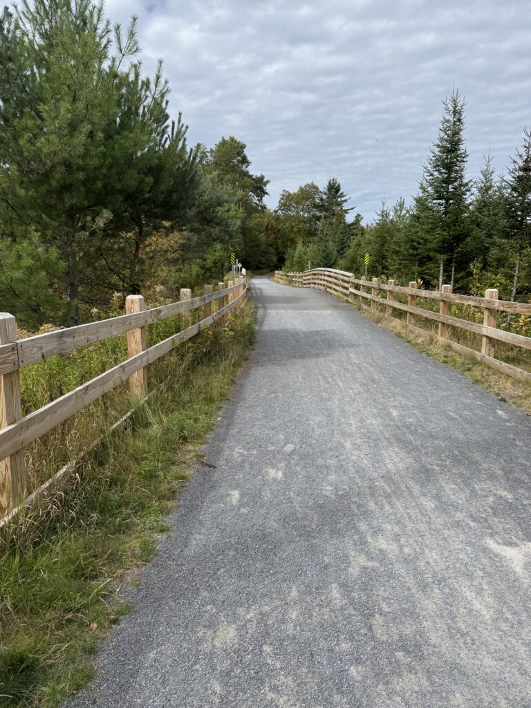 Entrance to the Lake Placid bike trail in New York, surrounded by trees and greenery.
