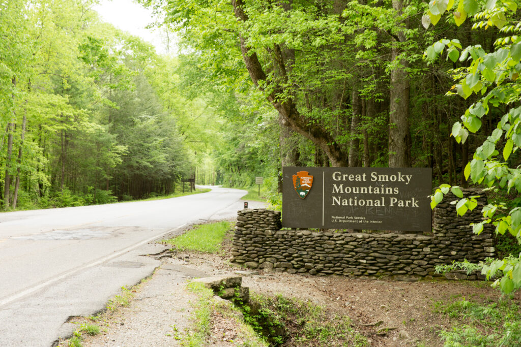 Wooden entrance sign welcoming visitors to Smoky Mountains National Park, surrounded by trees.
