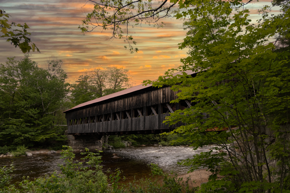 Side view of the Albany Covered Bridge spanning the Swift River, surrounded by summer greenery along the Kancamagus Highway in New Hampshire.
