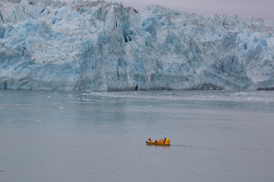 Small tour boat in front of Hubbard Glacier in Alaska, showing the immense scale of the towering blue ice wall.
