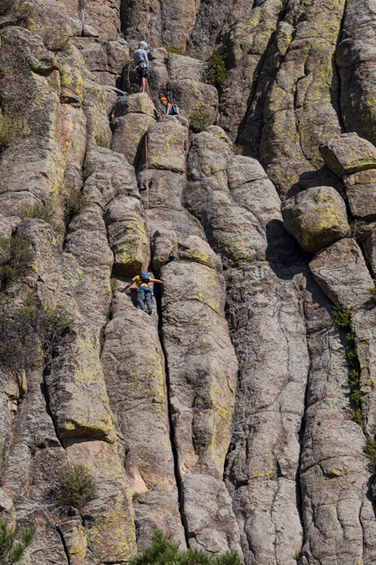 Three rock climbers ascending the steep face of Devil’s Tower in Wyoming under clear blue skies
