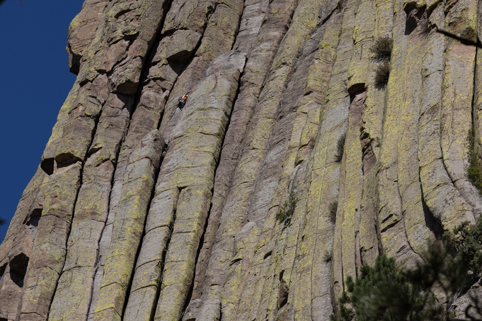 Tiny orange-clad rock climber scaling the sheer vertical face of Devil’s Tower in Wyoming