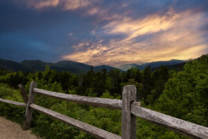 Wide mountain view from an overlook near Kancamagus Pass showing rolling green ridges of the White Mountains under summer haze.