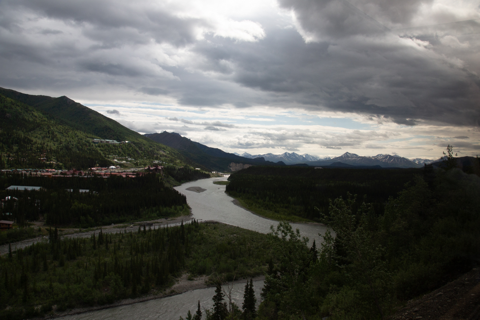 Evening light reflecting on the Chena River in Fairbanks, Alaska, with trees and buildings along the riverbank.
