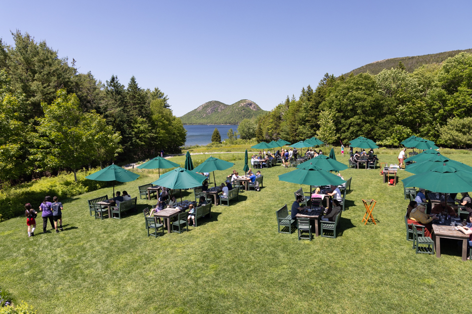 Visitors enjoying tea and popovers on the lawn at Jordan Pond House overlooking Jordan Pond and the Bubble Mountains in Acadia National Park.
